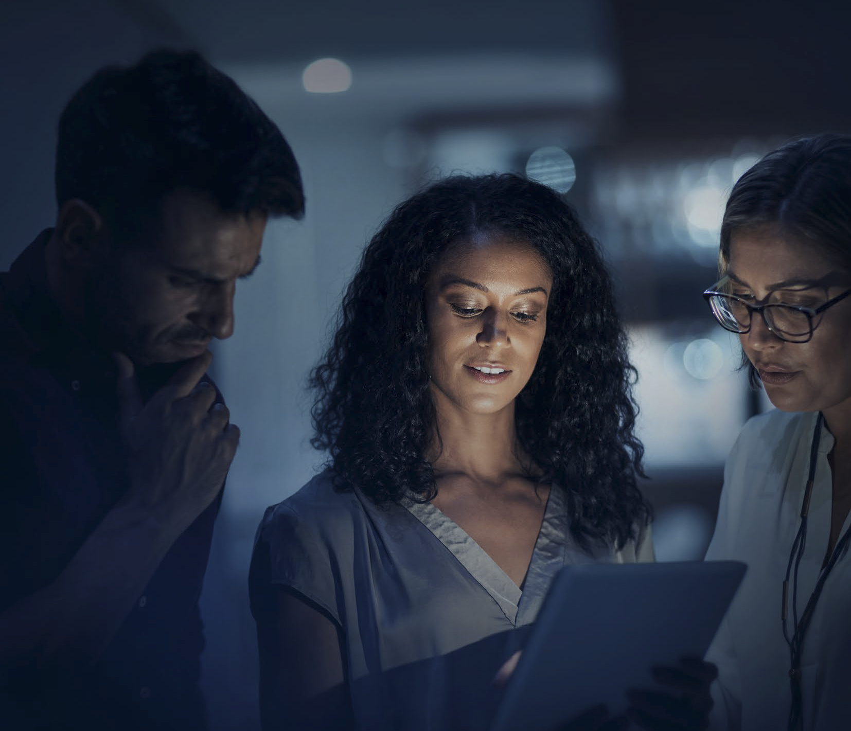 Um homem e 2 mulheres olhando para baixo olhando para tablete